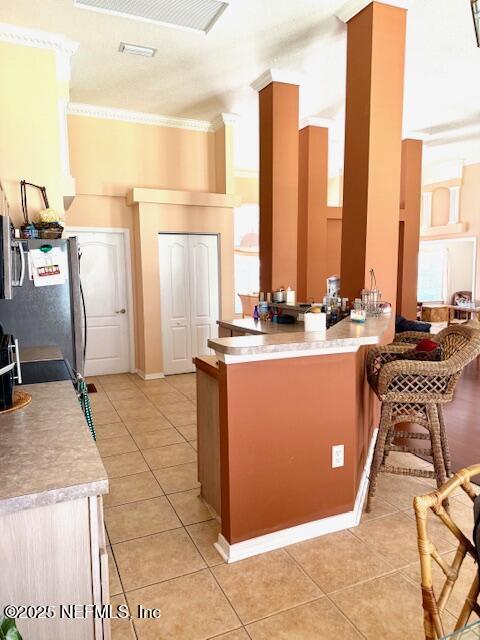 1837 The Glades Rd, Middleburg, FL 32068 - kitchen with freestanding refrigerator, light tile patterned floors, a breakfast bar area, crown molding, and light countertops