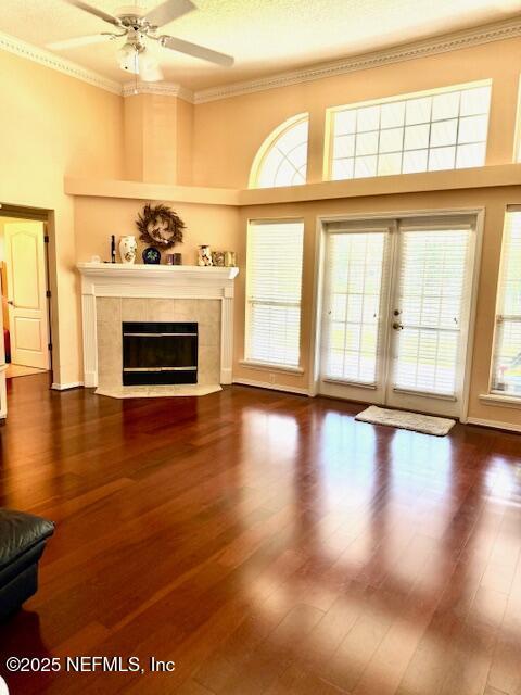 1837 The Glades Rd, Middleburg, FL 32068 - unfurnished living room featuring a tiled fireplace, ceiling fan, wood finished floors, ornamental molding, and a towering ceiling