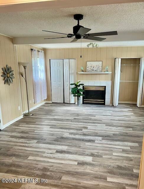 unfurnished living room with a textured ceiling, ceiling fan, wood-type flooring, a fireplace, and wood walls