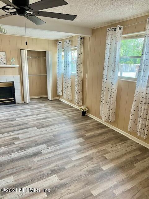 unfurnished living room with wood walls, wood-type flooring, a textured ceiling, and a tile fireplace