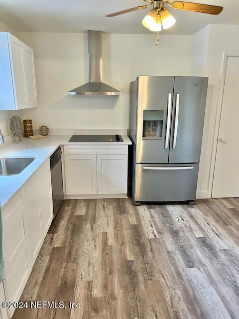 kitchen with sink, wall chimney range hood, appliances with stainless steel finishes, white cabinets, and light wood-type flooring