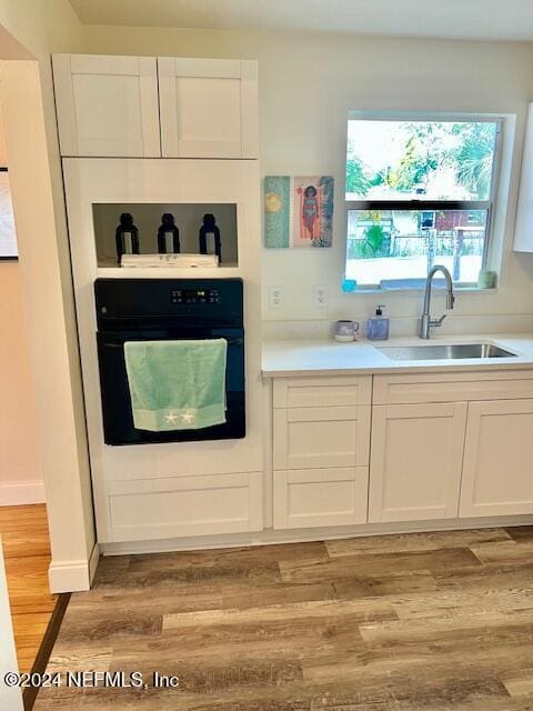 kitchen with white cabinets, sink, oven, and light hardwood / wood-style floors