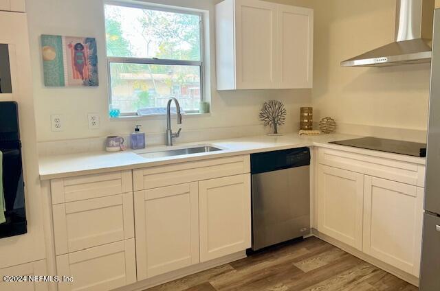 kitchen featuring sink, wall chimney range hood, wood-type flooring, white cabinets, and black appliances