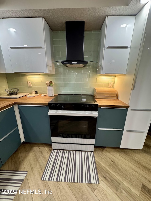 kitchen featuring wall chimney range hood, range, decorative backsplash, white cabinets, and light wood-type flooring