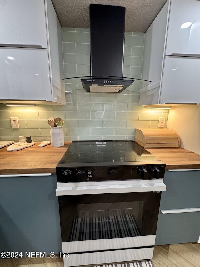 kitchen with stainless steel range with electric stovetop, wall chimney exhaust hood, decorative backsplash, and light wood-type flooring