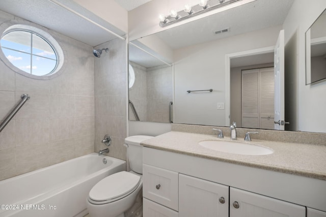 full bathroom with a textured ceiling, vanity, toilet, and tiled shower / bath