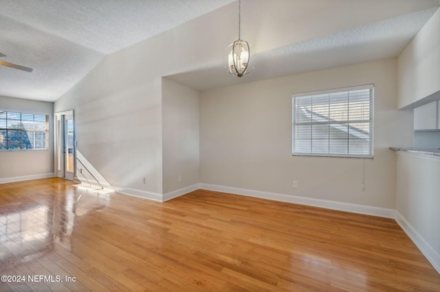 spare room with lofted ceiling, a textured ceiling, light hardwood / wood-style flooring, and a healthy amount of sunlight