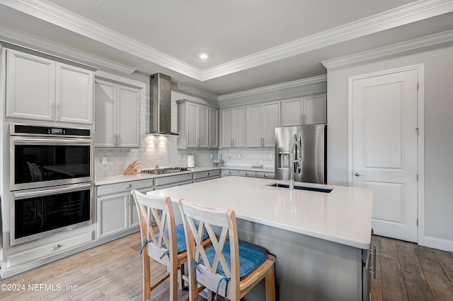 kitchen with a kitchen island with sink, wall chimney range hood, decorative backsplash, a kitchen bar, and stainless steel appliances