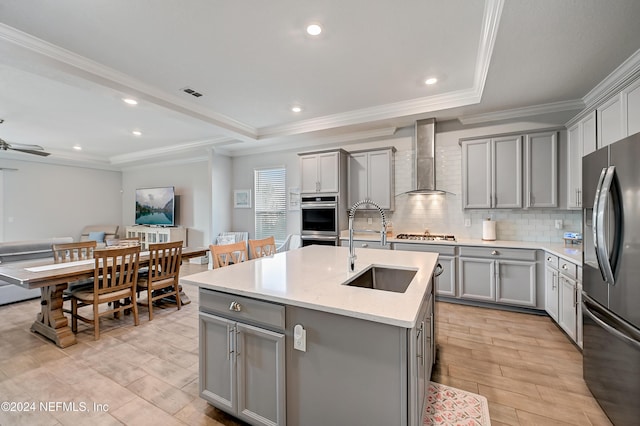 kitchen with gray cabinetry, wall chimney range hood, a kitchen island with sink, and appliances with stainless steel finishes