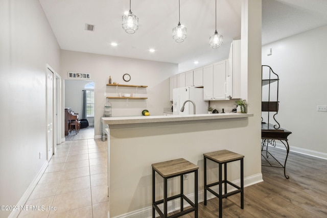 kitchen with white cabinetry, white fridge with ice dispenser, kitchen peninsula, decorative light fixtures, and a breakfast bar