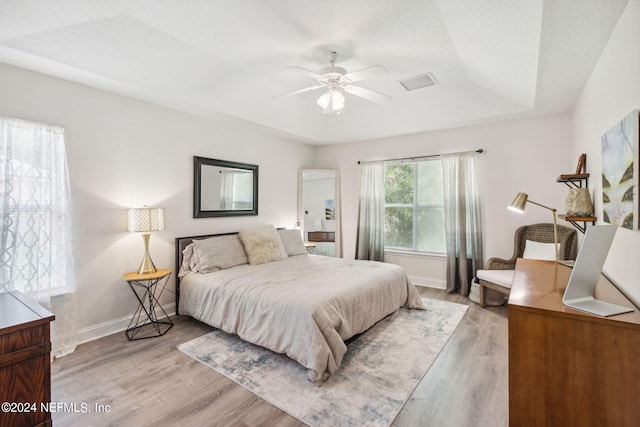 bedroom with ceiling fan, light hardwood / wood-style floors, and a tray ceiling