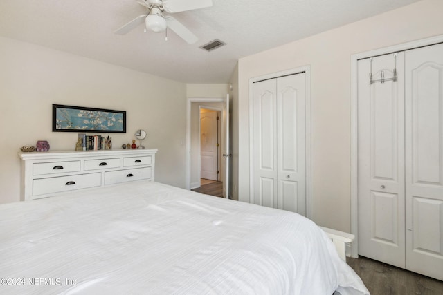 bedroom with ceiling fan, dark hardwood / wood-style flooring, and two closets