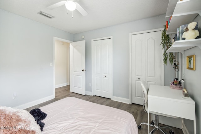 bedroom with a textured ceiling, ceiling fan, dark wood-type flooring, and multiple closets