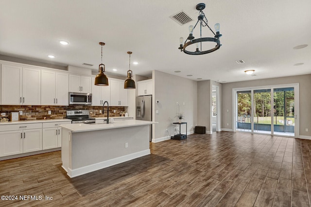 kitchen with stainless steel appliances, a kitchen island with sink, decorative light fixtures, an inviting chandelier, and white cabinets