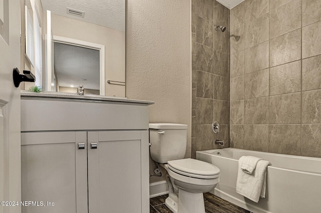 full bathroom with toilet, vanity, a textured ceiling, and tiled shower / bath