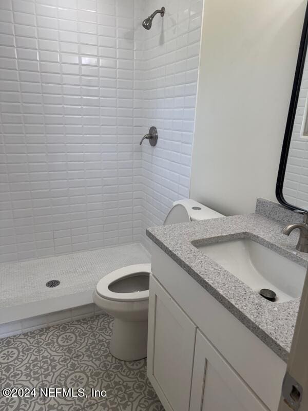 bathroom with tiled shower, vanity, toilet, and tile patterned flooring