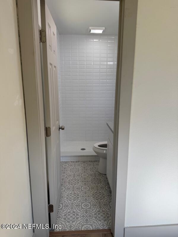 bathroom featuring tiled shower, tile patterned floors, vanity, and toilet