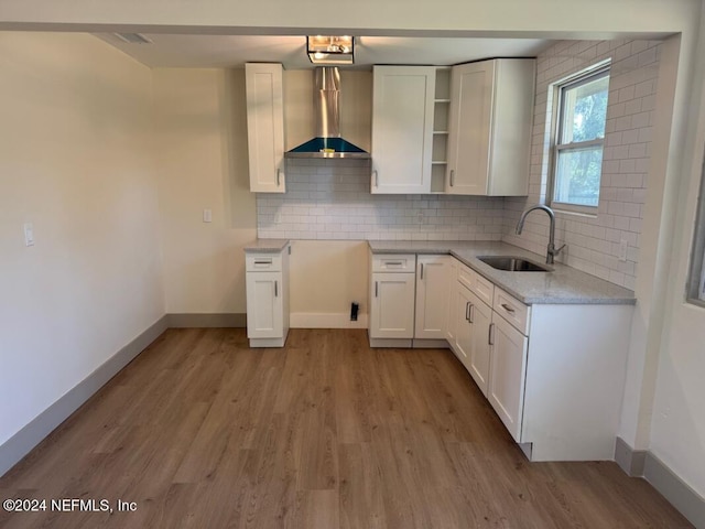 kitchen with light stone countertops, wall chimney range hood, sink, light hardwood / wood-style flooring, and white cabinets