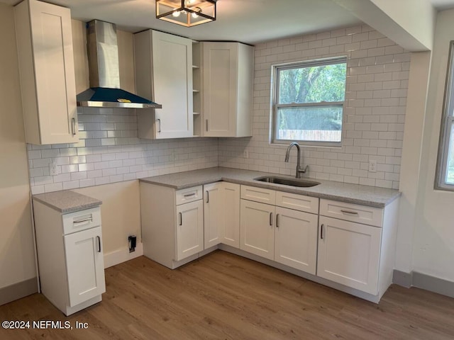 kitchen with white cabinets, light wood-type flooring, wall chimney range hood, and sink