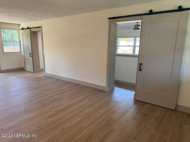 empty room with ceiling fan, a barn door, and light hardwood / wood-style flooring