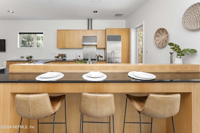 kitchen featuring a kitchen bar, ventilation hood, built in refrigerator, and sink