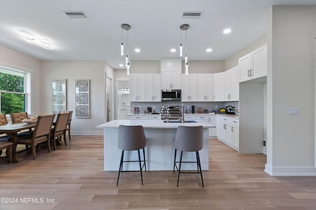 kitchen with tasteful backsplash, stainless steel appliances, a kitchen island with sink, pendant lighting, and white cabinetry