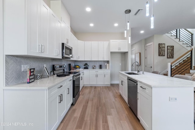 kitchen featuring appliances with stainless steel finishes, decorative light fixtures, white cabinetry, and light stone counters