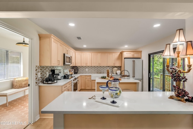 kitchen featuring appliances with stainless steel finishes, light brown cabinetry, tasteful backsplash, and decorative light fixtures