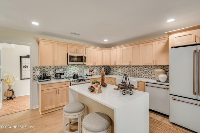 kitchen with light brown cabinetry, a center island, stainless steel appliances, and a breakfast bar area