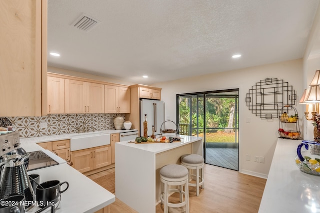 kitchen featuring a kitchen bar, an island with sink, backsplash, white appliances, and sink