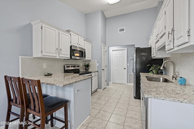 kitchen with a kitchen bar, stainless steel appliances, sink, white cabinetry, and light tile patterned flooring