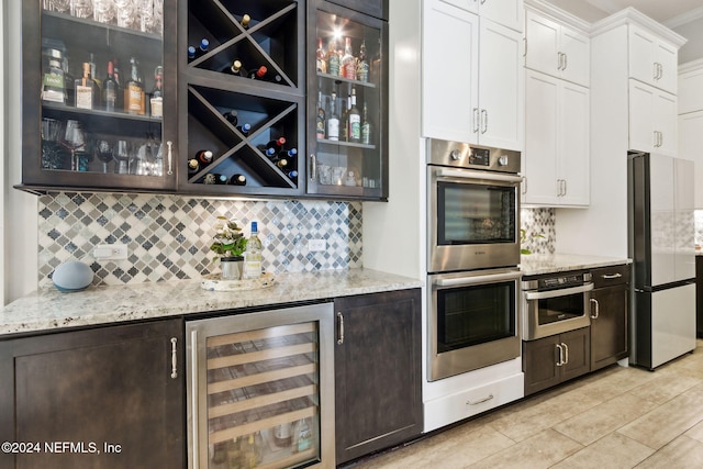 bar featuring decorative backsplash, appliances with stainless steel finishes, light stone countertops, white cabinets, and wine cooler