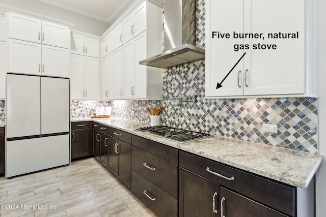 kitchen with wall chimney exhaust hood, stainless steel gas cooktop, light stone counters, white fridge, and white cabinets