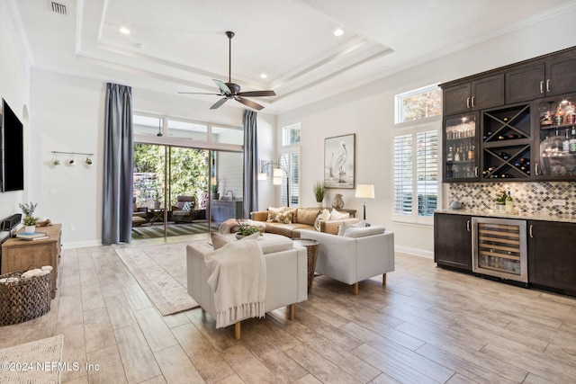 living room featuring bar area, light hardwood / wood-style flooring, beverage cooler, and a tray ceiling