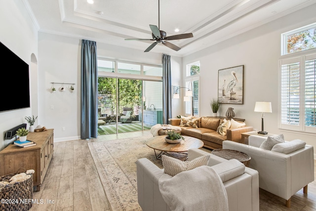 living room featuring a tray ceiling, crown molding, plenty of natural light, and light wood-type flooring