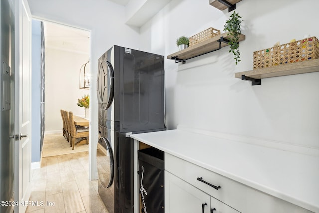 laundry area featuring stacked washer / dryer, light hardwood / wood-style flooring, and cabinets