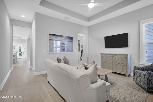 living room featuring ceiling fan, light hardwood / wood-style floors, and a tray ceiling