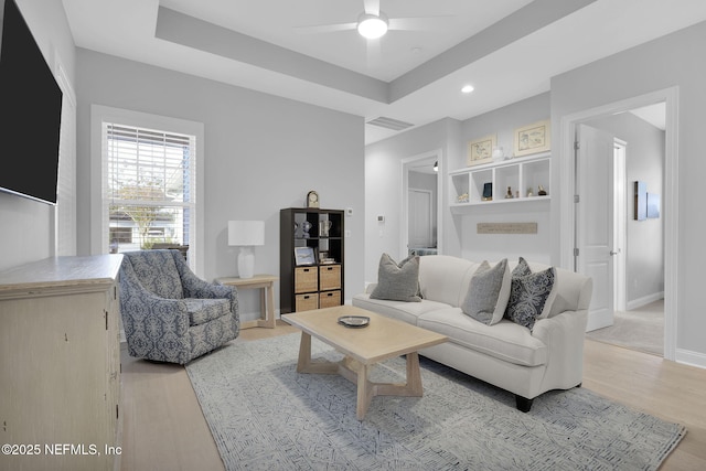 living room featuring ceiling fan, a raised ceiling, and light hardwood / wood-style flooring