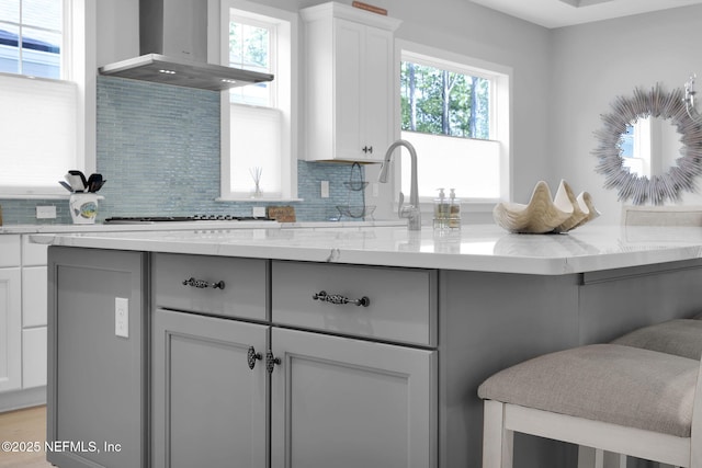 kitchen with exhaust hood, white cabinetry, tasteful backsplash, sink, and light stone counters