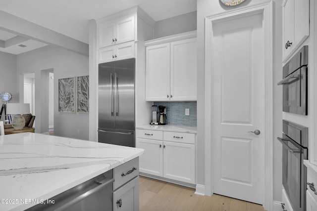 kitchen with white cabinets, appliances with stainless steel finishes, backsplash, light wood-type flooring, and light stone counters