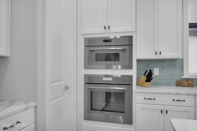 kitchen featuring white cabinetry, stainless steel double oven, light stone countertops, and tasteful backsplash