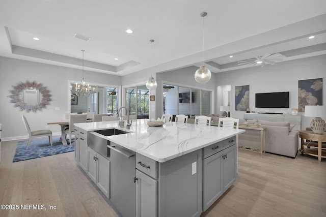 kitchen with a raised ceiling, a center island with sink, pendant lighting, and stainless steel dishwasher