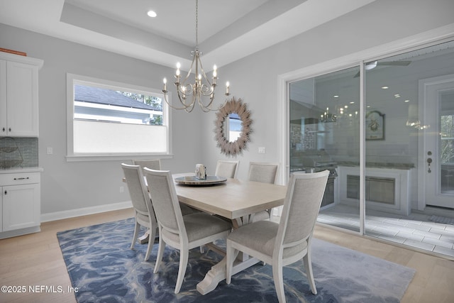 dining area with a raised ceiling, light hardwood / wood-style flooring, and an inviting chandelier