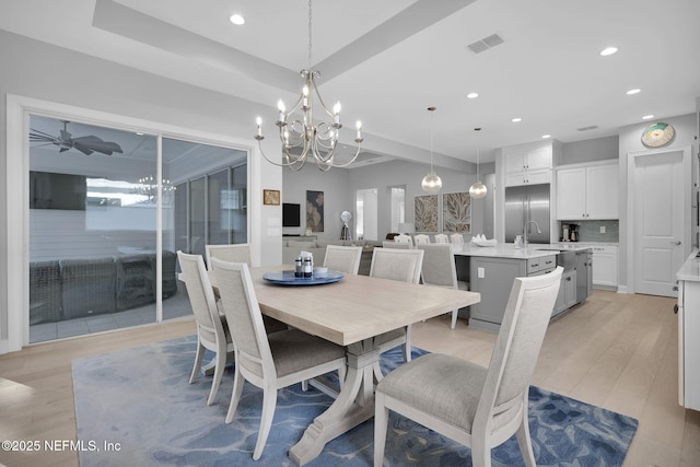 dining space with ceiling fan with notable chandelier, sink, a tray ceiling, and light hardwood / wood-style flooring