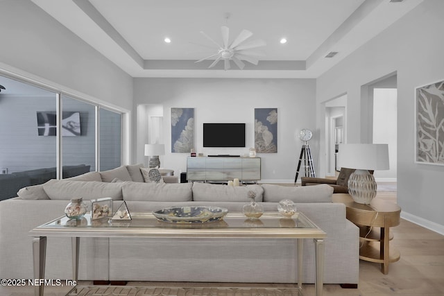 living room with ceiling fan, light hardwood / wood-style floors, and a tray ceiling