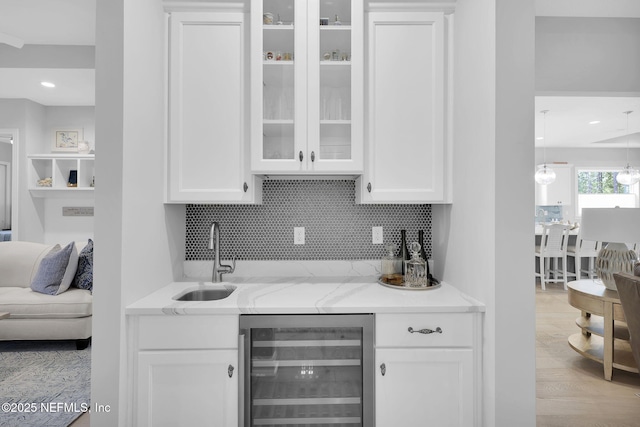 bar with tasteful backsplash, white cabinetry, sink, light stone counters, and wine cooler