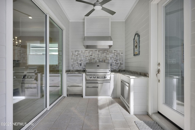 kitchen featuring ceiling fan with notable chandelier, backsplash, and wall chimney range hood