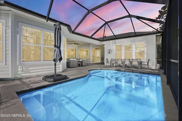 pool at dusk with a lanai, a patio area, and ceiling fan