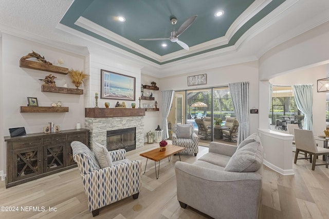 living room featuring a tray ceiling, a fireplace, light hardwood / wood-style floors, and ornamental molding