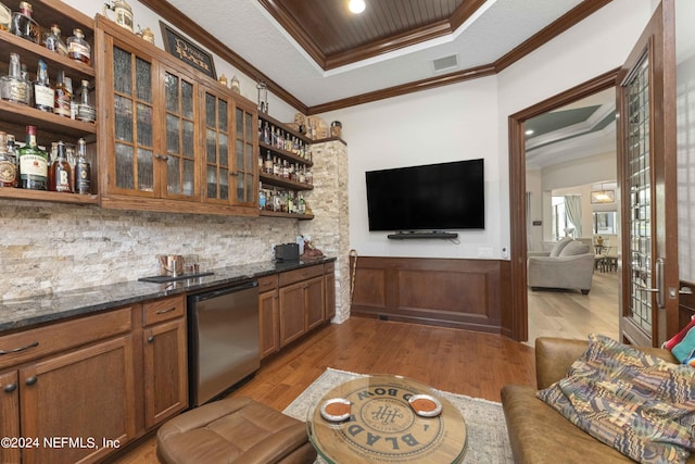 bar with backsplash, stainless steel dishwasher, dark stone counters, crown molding, and hardwood / wood-style floors